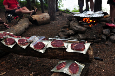 Steaks ready to cook, veggies already cooking on the fire